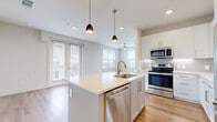 Located in Irving, TX, this well-appointed 2-bedroom, 2-bathroom residence offers a thoughtfully designed single-level layout. The open-concept living and kitchen area serves as the heart of the home, where warm light wood flooring, recessed lighting, and large windows with outdoor views create a bright and welcoming atmosphere. A ceiling fan adds comfort to the living space, which also features access to a balcony through glass doors.

The kitchen is a standout, boasting a central island with a built-in sink, pendant lighting, sleek white cabinetry, quartz countertops, a subway tile backsplash, and a full suite of stainless steel appliances including a refrigerator, range, microwave, and dishwasher.

Both bedrooms are generously sized and feature ceiling fans and plush carpeting. The second bedroom offers triple windows that flood the room with natural light. The primary bedroom connects directly to an en-suite bathroom with white cabinetry, a single vanity, wood-look flooring, and access to a dedicated walk-in closet complete with built-in shelving and hanging rods. A second full bathroom serves the additional bedroom. Two closets provide ample storage throughout the home.