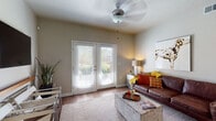 This single-floor residence is thoughtfully designed with a cohesive aesthetic and practical layout. The living area serves as the heart of the home, featuring warm hardwood-style flooring, a ceiling fan, and a set of French doors that fill the room with natural light and provide outdoor access. The open-concept kitchen is a functional standout, outfitted with rich dark cabinetry, granite-look countertops, stainless steel appliances including a refrigerator, range, and microwave, plus a dishwasher. A breakfast bar with seating and an adjacent dining area make it ideal for both everyday meals and entertaining. The bedrooms offer plush carpeting, natural light from well-positioned windows, and ample space. One room functions as a flexible home office or secondary bedroom, complete with a work desk and seating area. The bathrooms maintain a consistent design language, featuring dark wood vanities with granite-style countertops and full tub-shower combinations with curved curtain rods. A walk-in closet area with open shelving provides generous storage near one of the bathrooms. Neutral warm-gray tones flow throughout the space, creating a calm, unified ambiance well-suited to a variety of interior styles.