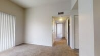 This single-story residence in Las Cruces, New Mexico presents a practical and well-organized layout with a neutral color palette throughout. The living area is anchored by plush wall-to-wall carpeting and features a sliding glass door dressed with vertical blinds, allowing generous natural light to fill the space while providing access to an outdoor area.

The kitchen is thoughtfully equipped with warm oak cabinetry, light countertops, and a mosaic tile backsplash that adds a subtle decorative detail. Black appliances, including a refrigerator and electric range, pair with a white dishwasher, offering a full complement of cooking and storage conveniences. Wood-look vinyl flooring runs throughout the kitchen, providing durability and easy maintenance.

The bedrooms feature soft carpeting and neutral walls, with at least one room benefiting from a ceiling fan and a window fitted with blinds for ventilation and light control. A hallway connects the rooms, with louvered closet doors providing organized storage. The bathroom includes an oak vanity with ample counter space, a large mirror, a shower-tub combination, and wood-look flooring, completing the functional interior of this Las Cruces home.