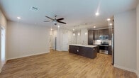 This single-story space showcases a contemporary open-concept design that seamlessly integrates the living area and kitchen. Wood-look flooring flows throughout the main living spaces, complementing the neutral gray-toned walls and creating a warm, cohesive aesthetic.

The kitchen is a standout feature, centered around a generously sized island with a sleek white quartz countertop, an undermount sink, and pendant lighting overhead. Dark espresso-toned shaker cabinetry extends to the ceiling, providing ample storage, while subway tile backsplash and a full suite of stainless steel appliances — including a refrigerator, range, and built-in microwave — complete the space. A dedicated in-unit laundry area is conveniently accessible from the kitchen corridor.

The living area is bright and airy, with multiple windows fitted with blinds allowing natural light to fill the room. A ceiling fan adds comfort, and a door provides additional access to the exterior.

The bedroom is a comfortable, well-lit space with its own ceiling fan and window. The bathroom features large-format tile flooring, a dual-sink white vanity with a wide mirror, and a clean, bright finish throughout. The overall ambiance is modern, fresh, and move-in ready.