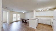Located at 801 S German Ln in Conway, Arkansas, this one-bedroom, one-bathroom unit is thoughtfully laid out across a single floor. The heart of the home is a combined living, dining, and kitchen space that feels open and connected. The kitchen features white cabinetry, a peninsula with a built-in sink, track lighting, and white appliances including a range and refrigerator — all set against light hardwood-style flooring that runs throughout the unit. The dining and living area is bathed in natural light, courtesy of a set of French doors that open to the outside, complemented by a ceiling fan overhead. The bedroom is a comfortable, well-lit room with a large window offering views of surrounding greenery and includes access to a walk-in closet, providing ample storage. Additional closets further enhance the unit's storage capacity. The bathroom is designed with accessibility in mind, featuring an open vanity with a mirror, grab bars, and hardwood-style flooring consistent with the rest of the unit. A dedicated utility room rounds out the layout. The overall aesthetic is clean and neutral, with light walls and warm flooring creating a bright, inviting atmosphere throughout.