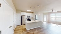 This single-floor unit presents a clean, contemporary design with a cohesive neutral color palette and light wood-look flooring carried consistently throughout the space. The open-concept kitchen and living area serves as the heart of the unit, where a central island with a white quartz countertop and an integrated sink anchors the layout. The kitchen is equipped with stainless steel appliances, including a refrigerator, electric range, and microwave, complemented by crisp white shaker-style cabinetry. Pendant lighting with glass globe fixtures hangs above the island, adding a refined touch. The adjacent living area is generously proportioned, receiving ample natural light through large windows fitted with horizontal blinds, and is fitted with a ceiling fan overhead.

The bedrooms continue the light, airy aesthetic, each featuring wood-look flooring, neutral walls, ceiling fans, and windows that bring in natural light and exterior views. Two bathrooms serve the unit: one features a walk-in tiled shower with large-format gray tile, while the other includes a separate water closet. Both bathrooms are appointed with white shaker vanities, white countertops, brushed nickel hardware, and wood-look flooring, maintaining a consistent, modern finish throughout.