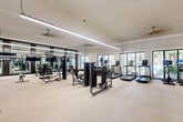 Located at 290 Courtney Lakes Cir in West Palm Beach, FL, this generously sized fitness center offers a comprehensive workout environment spread across a single, open floor. The space is designed with a clean, modern aesthetic, featuring light neutral carpeting, crisp white walls, and crown molding that lend a polished, upscale feel throughout.

The facility is well-lit by a combination of sleek linear pendant lighting and recessed ceiling fixtures, while multiple ceiling fans ensure comfortable airflow during intense workouts. Large windows and glass doors line the perimeter, flooding the interior with abundant natural light and offering views of lush outdoor greenery and what appears to be a pool area beyond.

Floor-to-ceiling mirrors are strategically positioned along one wall, visually expanding the space and providing users with proper form feedback. The equipment layout is thoughtfully organized, with a dedicated cardio zone housing multiple treadmills and a stationary bike, a strength training area featuring a variety of cable and resistance machines, and a free weights section with a full dumbbell rack and adjustable benches.

A functional training zone near the entrance is stocked with kettlebells, medicine balls, stability balls, resistance bands, and a Pilates-style reformer, supporting a wide range of fitness modalities. The space is accessible via glass entry doors and is clearly designed to serve as a premium amenity for residents of the community.