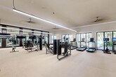 Located at 290 Courtney Lakes Cir in West Palm Beach, FL, this generously sized fitness center offers a comprehensive workout environment spread across a single, open floor. The space is designed with a clean, modern aesthetic, featuring light neutral carpeting, crisp white walls, and crown molding that lend a polished, upscale feel throughout.

The facility is well-lit by a combination of sleek linear pendant lighting and recessed ceiling fixtures, while multiple ceiling fans ensure comfortable airflow during intense workouts. Large windows and glass doors line the perimeter, flooding the interior with abundant natural light and offering views of lush outdoor greenery and what appears to be a pool area beyond.

Floor-to-ceiling mirrors are strategically positioned along one wall, visually expanding the space and providing users with proper form feedback. The equipment layout is thoughtfully organized, with a dedicated cardio zone housing multiple treadmills and a stationary bike, a strength training area featuring a variety of cable and resistance machines, and a free weights section with a full dumbbell rack and adjustable benches.

A functional training zone near the entrance is stocked with kettlebells, medicine balls, stability balls, resistance bands, and a Pilates-style reformer, supporting a wide range of fitness modalities. The space is accessible via glass entry doors and is clearly designed to serve as a premium amenity for residents of the community.