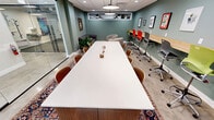 This 390-square-foot space efficiently combines multiple functionalities into a single-floor layout. The main area features a large white conference table, perfect for collaborative meetings or group work sessions. Along one wall, a sleek wooden counter serves as a workspace, complemented by colorful ergonomic chairs that add a playful touch to the professional environment. The sage green accent wall displays a curated collection of framed artwork, enhancing the room's aesthetic appeal.

Adjacent to the main area, a glass-walled room offers additional workspace or a private meeting area, maintaining an open feel while providing separation when needed. The space also includes a cozy lounge area, featuring a plush leather Chesterfield sofa, a round wooden coffee table, and a vibrant area rug that adds warmth to the concrete flooring.

Lighting is thoughtfully designed with a combination of recessed ceiling lights and large pendant fixtures, ensuring ample illumination throughout. The dropped ceiling with acoustic tiles likely aids in noise reduction, making the space suitable for various activities. High windows allow natural light to filter in, contributing to a bright and airy atmosphere.

This versatile space successfully balances functionality with style, creating an environment that encourages both productivity and comfort in a compact urban setting.