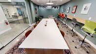 This 390-square-foot space efficiently combines multiple functionalities into a single-floor layout. The main area features a large white conference table, perfect for collaborative meetings or group work sessions. Along one wall, a sleek wooden counter serves as a workspace, complemented by colorful ergonomic chairs that add a playful touch to the professional environment. The sage green accent wall displays a curated collection of framed artwork, enhancing the room's aesthetic appeal.

Adjacent to the main area, a glass-walled room offers additional workspace or a private meeting area, maintaining an open feel while providing separation when needed. The space also includes a cozy lounge area, featuring a plush leather Chesterfield sofa, a round wooden coffee table, and a vibrant area rug that adds warmth to the concrete flooring.

Lighting is thoughtfully designed with a combination of recessed ceiling lights and large pendant fixtures, ensuring ample illumination throughout. The dropped ceiling with acoustic tiles likely aids in noise reduction, making the space suitable for various activities. High windows allow natural light to filter in, contributing to a bright and airy atmosphere.

This versatile space successfully balances functionality with style, creating an environment that encourages both productivity and comfort in a compact urban setting.