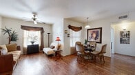This single-floor residence offers a cohesive and inviting layout designed for comfortable everyday living. The open-concept living and dining area serves as the heart of the home, featuring rich hardwood flooring that extends throughout the main living spaces. The living room is bathed in natural light through windows dressed with elegant draped valances, and is complemented by a ceiling fan overhead. A seamless transition leads to the dining area, where a pendant light illuminates a glass-top table surrounded by ornate upholstered chairs, with decorative wall sconces and framed artwork adding a refined touch.

The kitchen is equipped with deep-toned wood cabinetry, light countertops, a gas range, and a double-basin sink, offering ample storage and preparation space. Tile flooring grounds the kitchen and continues into the utility areas.

The bedroom is a comfortable retreat, featuring plush carpeting, a ceiling fan, and windows that allow natural light to filter in. Two full bathrooms serve the residence — the primary bathroom includes a double-sink vanity with rich wood cabinetry, a framed mirror, and a tub-shower combination, with direct access to a walk-in closet. The second bathroom mirrors the same quality cabinetry and finishes. A dedicated laundry room with a stacked washer and dryer unit rounds out the functional amenities of this well-designed home.
