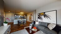 This well-appointed single-floor residence showcases a thoughtfully designed open-concept layout that seamlessly connects the kitchen, dining, and living areas. Rich hardwood flooring flows throughout the main living spaces, anchoring the contemporary aesthetic.

The gourmet kitchen is a standout feature, equipped with stainless steel appliances, a tile mosaic backsplash, gray shaker-style cabinetry extending to the ceiling, and a generous granite-topped island with pendant lighting and an undermount sink. A dedicated dining area adjacent to the kitchen comfortably accommodates a round table and seating.

The living room is bright and inviting, benefiting from large windows that invite natural light and offer outdoor views. The space is accented by bold artwork and a mix of modern furnishings that complement the neutral gray tones of the walls.

The two bedrooms are calm and comfortable retreats, each featuring soft carpeting, generous closet space with sliding doors, and warm ambient lighting. The bathroom is clean and functional, finished with granite countertops, gray cabinetry, and a tiled shower.

Throughout the residence, a cohesive palette of grays, whites, and warm wood tones creates a polished, modern atmosphere that is both practical and visually refined.