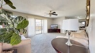 This single-floor residence offers a thoughtfully organized layout designed for comfortable everyday living. The expansive living room is finished with plush carpeting, a textured ceiling, and a ceiling fan, and is anchored by a large sliding glass door with vertical blinds that opens to a private outdoor balcony, filling the space with natural light and exterior views. A secondary seating area within the living space provides additional room for relaxation. The dining area features wood-look flooring, a counter-height table with upholstered chairs, and a decorative mirror that enhances the sense of openness. The galley-style kitchen is efficiently designed with dark cabinetry, white appliances including a range, microwave, refrigerator, and dishwasher, complemented by light countertops and wood-look flooring. Both bedrooms are carpeted and offer a tranquil retreat; one includes mirrored sliding closet doors, while the other provides a quiet, understated ambiance with a window for natural light. The full bathroom features a single-sink vanity with dark cabinetry, a combination tub and shower, and wood-look tile flooring. A dedicated in-unit laundry room accommodates a full-size washer and dryer, adding everyday convenience to this functional and comfortable residence.