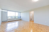 Located at 1219 Dundas St W in Mississauga, this 2-bedroom, 1-bathroom unit offers a functional and well-organized layout across a single floor. The living room is a standout feature, anchored by large floor-to-ceiling sliding windows that flood the space with natural light and frame pleasant views of the surrounding greenery and cityscape. Warm parquet wood flooring runs consistently throughout the living areas and both bedrooms, adding a classic character to the interior.

The kitchen is efficiently designed with grey cabinetry, granite-style countertops, white tile backsplash, tile flooring, and a full suite of appliances including an electric range and refrigerator. The primary bedroom is generously proportioned, offering ample space for furnishings, while the second bedroom features a dedicated window with outdoor views and baseboard heating. Both bedrooms benefit from natural light and parquet flooring. One bedroom includes a built-in sliding door closet for convenient storage.

The bathroom is clean and straightforward, featuring a tub-shower combo, a vanity with granite-style countertop, grey cabinetry, tile flooring, and a small privacy window. Two hallways connect the rooms, contributing to a practical flow throughout the unit.