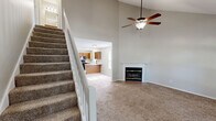 This two-story home in Columbia, Missouri offers three bedrooms and two full bathrooms across a well-organized layout. The main floor hosts the living room, kitchen, and one bathroom, while the upper level accommodates the bedrooms and second bathroom. The living room is a standout space, featuring soaring vaulted ceilings and a classic wood-mantled fireplace set against neutral walls with plush carpeting underfoot. The kitchen is efficiently laid out with warm oak cabinetry, light countertops, a double-basin sink beneath a window with outdoor views, and black appliances including a range, microwave, and dishwasher, alongside light wood-look flooring. The primary bedroom impresses with dramatic vaulted ceilings, a ceiling fan, and a pair of arched windows that flood the room with natural light and views of the surrounding greenery. The additional bedrooms also feature carpeted floors and arched or standard windows. Both bathrooms are functional and clean, each equipped with a tub-shower combo, vanity with sink, and tile-style flooring. A staircase connects the two floors, and two closets provide convenient storage throughout the home.