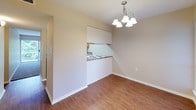 This single-floor residence is thoughtfully laid out across several well-defined areas. The entry foyer welcomes residents through a solid front door, flanked by a window that allows natural light to illuminate the warm hardwood-style flooring that extends through the main living and dining areas. A chandelier overhead adds a decorative touch to the dining space, which connects to the kitchen via a half-wall pass-through. The kitchen features oak cabinetry, granite-patterned countertops, a double stainless steel sink, a dishwasher, and a cooktop, offering practical functionality. The living room is carpeted and benefits from a sliding glass door fitted with vertical blinds, providing both natural light and access to an outdoor area with greenery views. Multiple bedrooms are carpeted and each equipped with dual bi-fold closets, providing ample storage. The bathrooms feature oak vanities with granite-patterned countertops, mirrored medicine cabinets, and a tub-shower combination. Neutral beige tones throughout the space create a cohesive, understated aesthetic suited for a variety of interior styles.