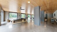 Located on First Street in Norwalk, CT, this expansive single-floor entertainment space offers a generous and open layout designed for both comfort and activity. The interior is defined by a compelling combination of textured stacked-stone walls, polished concrete floors, and a warm wood-plank ceiling that together create a refined yet relaxed atmosphere.

Large floor-to-ceiling openings along the perimeter flood the space with natural light and provide seamless views of the surrounding mature trees and greenery, blurring the line between indoors and outdoors. A ceiling fan and recessed lighting complement the natural illumination throughout.

The layout accommodates multiple functional zones. A seating area features a substantial sectional sofa with a solid wood frame alongside accent chairs, ideal for lounging. A billiards table serves as a central entertainment focal point, while a bar-height table with metal chairs provides a casual dining or gathering spot. A shuffleboard table adds to the recreational offerings. A wall-mounted flat-screen television is integrated into the stone wall, accompanied by built-in media storage below.

Structural columns with gray paneled detailing add architectural interest and help define zones within the open plan. The overall ambiance is contemporary and inviting, blending natural materials with modern furnishings to create a versatile and well-appointed gathering space.