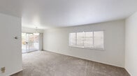 Located at 1812 W Riverside Ave in Spokane, Washington, this one-bedroom, one-bathroom unit offers a practical and well-organized single-floor layout. The open-concept living, dining, and kitchen area serves as the heart of the unit, with neutral-toned carpet underfoot and bright white walls that create a clean, airy atmosphere. A pendant light fixture adds a subtle decorative touch, while a sliding glass door leads directly to a private patio, allowing natural light to flow in and providing outdoor access. Multiple windows fitted with white horizontal blinds further brighten the space throughout. The bedroom is a comfortable, carpeted room featuring a built-in wall heater, a well-sized window for natural light, and access to a dedicated closet. The bathroom offers wood-look flooring and a white vanity with ample cabinet storage beneath a large mirror. Brushed nickel fixtures, including a towel bar and ring, lend a polished finish. A hallway connects the main living area to the private quarters, contributing to a functional flow throughout the unit. The overall design is straightforward and neutral, offering a versatile canvas well-suited to a range of interior styles.