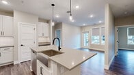 This single-floor residence showcases a contemporary design with a cohesive neutral palette, wood-look flooring, and crisp white millwork throughout. The open-concept kitchen serves as the centerpiece, featuring a large quartz-topped island with an undermount sink and matte black faucet, illuminated by pendant lighting. White shaker cabinetry — including glass-front upper cabinets — lines the walls alongside a classic subway tile backsplash. Stainless steel appliances, including a French door refrigerator, range, and microwave, complete the space. A dedicated built-in desk area and in-unit stacked washer and dryer are conveniently accessible from the kitchen.

The living area opens to a private balcony through a glass-panel door, with roller shades on surrounding windows providing adjustable natural light. Bedrooms are bright and well-proportioned, each with wood-look flooring and clean-lined five-panel doors with matte black hardware. The primary bathroom connects to a walk-in closet and includes a soaking tub. A second full bathroom offers a white vanity with quartz countertop and matching matte black fixtures, maintaining the home's consistent modern aesthetic throughout.