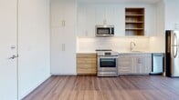 Located at 3009 W Leigh St in Richmond, Virginia, this single-floor unit showcases a clean, modern aesthetic throughout. The design emphasizes an open, airy feel with crisp white walls, recessed lighting, and consistent hardwood-style flooring that flows through the main living areas.

The kitchen is well-appointed with stainless steel appliances, including an electric range and built-in microwave. Two-toned cabinetry—combining white upper cabinets with warm wood-finish lower cabinets—adds visual depth, while a classic subway tile backsplash and open shelving provide both style and practicality.

The living area benefits from large windows offering views of the surrounding Richmond neighborhood, allowing generous natural light. A sliding barn door adds a contemporary architectural detail to one of the rooms, which also features hardwood-style flooring and a window with outdoor views. A separate carpeted room with a high clerestory window offers a quieter, more private setting.

The bathroom is finished with large-format floor tiles, subway tile surrounding the soaking tub and shower combination, and warm brass fixtures paired with a wood-toned vanity. The overall palette remains neutral and cohesive throughout, creating a calm and functional living environment.