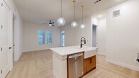 This thoughtfully designed home in Austin, TX offers a clean, modern aesthetic with high-quality finishes throughout. The open-concept layout connects the kitchen and living area seamlessly, creating a bright and inviting atmosphere. Light pours in through multiple windows, complementing the warm, light-toned herringbone hardwood flooring that flows consistently across the space.

The kitchen serves as the heart of the home, anchored by a central island with a crisp white quartz countertop, a farmhouse-style sink, and a matte black faucet. Warm wood cabinetry pairs elegantly with stainless steel appliances, including a side-by-side refrigerator with ice dispenser and built-in microwave. Three globe pendant lights with brass fixtures hang above the island, adding a refined touch. A built-in mudroom nook with open shelving and hooks provides convenient everyday storage.

Each of the three bedrooms features the same herringbone flooring and neutral wall tones, offering a calm and versatile canvas. The primary bedroom includes access to a well-appointed bathroom with warm wood vanity, matte black hardware, a framed mirror, and an adjacent walk-in closet with built-in shelving. A second bathroom features a soaking tub and shower combo surrounded by striking marble-look tile with matte black fixtures. A ceiling fan in the living area adds comfort, rounding out this polished Austin residence.