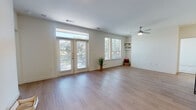 This single-story unit offers a thoughtfully designed open-concept layout finished with light wood-look flooring throughout the main living areas. The spacious living room is filled with natural light, courtesy of large French doors topped with transom windows and an additional side window fitted with blinds. A ceiling fan overhead and built-in shelving in the corner add functional detail to the airy space.

The kitchen is a standout feature, showcasing dark espresso cabinetry, a classic white tile backsplash, granite countertops, and a full suite of stainless steel appliances including a refrigerator, range, and microwave. A central island with a granite surface, undermount sink, and pendant lighting above provides seating and additional workspace, seamlessly connecting the kitchen to the living area.

Both bedrooms are carpeted and receive generous natural light through blinds-covered windows. The primary bathroom is well-appointed with a dual-sink vanity featuring granite countertops, dark cabinetry, a tiled tub-shower combination, and wood-look flooring. A second full bathroom mirrors this aesthetic with a tiled tub-shower and granite vanity. The overall ambiance is clean, modern, and move-in ready.