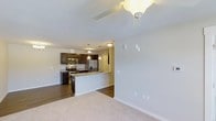 This single-story residence at 3400 Briercliff Dr in Greenville, NC, offers an open-concept design that integrates the living and kitchen areas into one cohesive, functional space. The living area features neutral-toned carpet and a ceiling fan, creating a comfortable and well-ventilated environment. Smooth, light-colored walls throughout contribute to a clean, airy ambiance.

The kitchen is a standout feature, outfitted with dark espresso cabinetry that provides a striking contrast against the lighter surroundings. A granite-topped peninsula serves as both a prep area and a casual dining or gathering space. Stainless steel appliances, including a refrigerator, microwave, and range, lend a modern, polished look. Pendant lighting above the peninsula adds focused illumination and a decorative touch, complementing the additional overhead lighting that keeps the space bright.

Dark hardwood-style flooring in the kitchen transitions to carpeting in the living area, clearly defining each zone while maintaining visual continuity. The overall layout and design elements combine practicality with contemporary style throughout this well-appointed single-floor home.