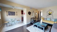 Located at 541 Randolph Road in Newport News, Virginia, this single-story home offers a thoughtfully arranged layout that balances comfort and character. The living area welcomes you with rich dark hardwood flooring, warm yellow-toned walls, and an abundance of natural light. A statement coffee table with industrial styling anchors the space, complemented by a plush yellow accent chair and decorative wall pieces that give the room a distinctive, eclectic personality. A ceiling fan overhead ensures year-round comfort. The living space flows seamlessly into a hallway that connects to additional rooms, maintaining an open and airy feel throughout. An archway leads to the kitchen and dining area, where light tile flooring creates a clean contrast to the darker hardwood in the main living space. The kitchen features rich dark wood cabinetry and a functional layout, while the adjacent dining nook provides an intimate space for meals. Decorative accents, including ornate mirrors, gear-shaped wall art, and curated accessories, lend the home a creative and inviting ambiance. With its open sightlines, cohesive design, and single-floor accessibility, this Newport News home offers both practicality and visual appeal.