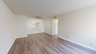 Located at 5675 Barnhill Dr in Jacksonville, FL, this single-floor unit offers three bedrooms and two bathrooms within a thoughtfully arranged floor plan. The combined living and dining area serves as the heart of the home, finished with warm wood-look laminate flooring that extends throughout the unit. A ceiling fan with light fixture keeps the space comfortable, while a pass-through window connects the living area directly to the kitchen, creating an open, communicative feel. The kitchen features white cabinetry and includes a refrigerator, maintaining a clean and functional aesthetic. Bedrooms are bright and well-proportioned, each featuring the same wood-look flooring, neutral cream-toned walls, and vertical blind-covered windows that invite natural light. Several bedrooms include closets, and the unit provides a total of four closets for generous storage throughout. The two bathrooms are finished in a crisp white palette — one features a full tub and shower with white subway tile surround and a white vanity, while the second offers a single vanity with mirror and tile flooring. Textured ceilings and clean white trim complete the interior. The layout, as seen in the dollhouse view, is efficiently organized with clear room separation and easy flow between spaces.