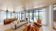 Located in the heart of Fort Myers, FL, this thoughtfully designed single-floor space combines contemporary architecture with warm, organic materials to create an inviting and sophisticated atmosphere. The interior living area features a striking wood-planked ceiling that adds warmth and texture, complemented by expansive floor-to-ceiling black-framed windows and glass doors that flood the space with natural light and provide seamless views of the outdoor terrace and city skyline. Natural fiber rugs, a live-edge teak coffee table, and a mix of neutral-toned and woven furnishings reinforce the space's organic aesthetic. A built-in shelving unit with integrated media display and a dining area with cane-back chairs round out the interior, offering both function and style. A standout feature is the dedicated outdoor living area, sheltered beneath a bold black pergola structure and adorned with string lights. This terrace is furnished with a generous modular sectional sofa and rustic teak stump side tables, all oriented to take full advantage of the sweeping views of Fort Myers' skyline and lush tropical palm canopy. An additional area showcases a dramatic large-format natural stone accent wall, adding an earthy, textural focal point. Together, these spaces deliver a cohesive blend of coastal-modern design and natural elegance.