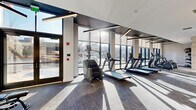 Located at 417 Callowhill Street in Philadelphia's vibrant Callowhill neighborhood, this modern fitness center offers a well-appointed exercise space designed for comprehensive workouts. The single-floor facility is thoughtfully laid out to accommodate a full range of cardio and strength training equipment.

Floor-to-ceiling glass curtain walls line one side of the room, flooding the interior with abundant natural light and offering open views of the surrounding streetscape. The interplay of sunlight across the textured carpet flooring creates a bright, energizing atmosphere throughout the day.

The cardio zone features multiple treadmills, elliptical trainers, stair climbers, and stationary bikes, all positioned to take advantage of the expansive window views. The strength training area is equipped with cable machines, a squat rack, adjustable benches, and a dedicated free weights section, complemented by large wall mirrors that enhance the sense of space.

Overhead, sleek linear LED lighting runs in parallel strips across the ceiling, reinforcing the contemporary aesthetic alongside warm wood-paneled accent walls at the rear. A separate glass-enclosed studio area provides additional space for focused training. The overall design is clean, modern, and functional, making this fitness center a well-equipped destination for residents and users in the heart of Philadelphia.