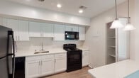 This single-floor home offers a thoughtfully designed layout with a blend of modern updates and functional living spaces. The spacious living area is highlighted by rich hardwood-style flooring and a ceiling fan, while wide sliding glass doors span nearly the full width of the room, flooding the space with natural light and offering direct views of a private backyard complete with a storage shed and fenced yard.

The kitchen is clean and contemporary, featuring white shaker-style cabinetry with brushed nickel hardware, light quartz countertops, a stainless steel sink, and black appliances including a range, over-the-range microwave, refrigerator, and dishwasher. Recessed lighting illuminates the workspace efficiently.

A secondary living or dining area with hardwood-style floors connects to the kitchen, offering closet access and flexible use. The bedroom is carpeted and bright, with multiple windows that bring in natural light and views of the surrounding greenery.

The bathrooms are finished with marble-style tile flooring and surround, a white vanity, and chrome fixtures, lending a clean and polished aesthetic. The layout, visible in the dollhouse view, flows logically from the main living spaces to the private rooms, making for a practical and comfortable single-level home.