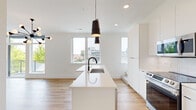Located at 2721 W 25th Ave in Denver's vibrant LoHi neighborhood, this contemporary three-bedroom, three-bathroom townhome spans three well-designed floors. The main level features an open-concept kitchen and living area finished with light hardwood flooring throughout. The sleek kitchen is anchored by a large white waterfall island with an integrated sink and matte black faucet, complemented by flat-panel white cabinetry that extends to the ceiling, stainless steel appliances, and modern pendant lighting. Multiple windows flood the space with natural light and offer neighborhood views. The living area opens to a private balcony through floor-to-ceiling glass doors, topped with a striking Sputnik chandelier. The three bedrooms feature plush carpeting and generous windows, with the primary bedroom offering a well-proportioned layout and closet access. Each of the three bathrooms is finished in a crisp, modern style — one featuring a glass-enclosed tile shower with matte black fixtures and a floating vanity. Matte black hardware accents appear consistently throughout, lending a cohesive, contemporary feel. The top floor opens to a spacious rooftop deck with composite decking and sleek metal railings, providing panoramic views of the Denver skyline — a standout feature of this well-appointed home.