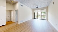 Located at 2281 N Lois Ave in Tampa, FL, this 2-bedroom, 3-bathroom unit showcases a contemporary industrial aesthetic defined by exposed concrete ceilings, light-toned wood flooring, and a clean, neutral color palette throughout. The single-floor layout maximizes functional living space across a well-organized floor plan.

The open-concept kitchen is a standout feature, equipped with flat-front white cabinetry extending to ceiling height, a marble-style tile backsplash, stainless steel appliances including a French door refrigerator, built-in oven, and dishwasher, a wall-mounted range hood, and a central island with a white quartz countertop. The adjacent living area benefits from large sliding glass doors that invite abundant natural light and provide direct access to an outdoor balcony with greenery views. A ceiling fan adds functional comfort.

Both bedrooms feature light wood flooring, exposed concrete ceilings, and windows overlooking outdoor green spaces. The spacious primary bedroom offers a notably generous footprint. The three bathrooms are finished in a modern style — one includes a glass-enclosed walk-in shower with a built-in bench and matte black fixtures, while another features a soaking tub with a tiled surround, dark countertops, and white cabinetry.