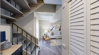 Located at 901 St. Johns Wood Drive in Richmond, Virginia, this two-story loft-style space offers a smart and efficient layout spread across two levels. The main floor features an open-concept living and kitchen area with warm wood-look flooring, exposed beam ceilings painted white for a modern industrial aesthetic, and a compact kitchen with a breakfast bar and built-in shelving. A striking dark metal staircase serves as both a functional and architectural focal point, connecting the main level to the upper floor. The upper level transitions to plush carpeting and houses the bedroom, which features high ceilings that enhance the sense of volume, a large closet with bifold doors, and a cozy, well-appointed ambiance. The full bathroom is finished with classic white subway tile surrounding a full soaking tub and shower combination, complemented by wood-look flooring for a clean, contemporary feel. A dedicated office and laundry area add practical functionality to the overall layout. Neutral warm and cool gray tones are carried throughout both floors, creating a cohesive and calming atmosphere. The thoughtful use of vertical space and multi-functional rooms makes this two-level space a well-organized and versatile place to live and work.