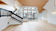 This thoughtfully designed two-story home offers an impressive layout across two floors, with the main level providing the larger share of living space. The interior is defined by striking architectural details, most notably the warm wood-planked and beam-accented ceilings that span the main living areas, lending a sense of warmth and craftsmanship throughout.

The main living room is a true showpiece, featuring soaring ceilings with exposed wood beams, light hardwood flooring, and a bold dark-tiled fireplace as a focal point. A dramatic floor-to-ceiling glass wall frames views of an enclosed outdoor courtyard with sleek black metal railings, filling the space with abundant natural light. A sculptural staircase with black metal railings connects the two floors seamlessly.

The kitchen is well-appointed with two-tone cabinetry in white and gray, gold hardware, quartz countertops, a central island with a cooktop, and stainless steel appliances including a dishwasher and wall oven. Windows above the sink bring in natural light and garden views.

The home includes three bedrooms, each with hardwood flooring and closet storage, including a generously sized primary suite. Six well-finished bathrooms feature clean white vanities, tub-shower combinations, and hardwood-style flooring. A dedicated laundry room with full-size washer and dryer adds everyday convenience. The exterior courtyard, accessible from the main living area, offers a private outdoor retreat surrounded by the home's two-story facade.