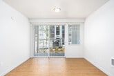This single-floor residence showcases a clean, modern design throughout its well-organized layout. The kitchen serves as a central highlight, featuring a two-toned design with white upper cabinetry and dark lower cabinets, complemented by white quartz countertops, stainless steel appliances including a refrigerator, range, and microwave, and a central island with an integrated sink illuminated by stylish pendant lighting. Light bamboo-style hardwood flooring flows through the kitchen and main living areas, creating a cohesive, contemporary feel.

The living area is bright and open, benefiting from natural light through a large sliding glass door fitted with vertical blinds that provides outdoor access. Bedrooms are carpeted for comfort, with one featuring multiple windows, a ceiling fan, and direct access to a bathroom with a dark-toned vanity. A generously sized walk-in closet with wire shelving systems offers substantial storage capacity.

The bathroom includes a full tub-shower combination with brushed nickel grab bars, reflecting an accessibility-conscious design. The hallway connects all rooms efficiently, and the overall color palette of crisp whites and neutral tones creates a bright, clean ambiance throughout.