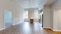 This single-floor unit blends historic architectural character with modern finishes throughout its well-organized layout. The main living and kitchen area immediately draws attention with its striking pressed-tin ceiling, a decorative coffered design that adds depth and elegance to the space. Tall, arched windows flood the room with natural light and offer views of the surrounding brick exteriors, reinforcing the building's classic urban character. Wainscoting panels line the lower walls, complementing the warm hardwood-style flooring that runs throughout the main area.

The kitchen is thoughtfully designed with white shaker cabinetry, light countertops, and a full suite of stainless steel appliances, including a range, dishwasher, microwave, and refrigerator. A central island provides additional prep and seating space, with a peninsula-style counter further separating the kitchen from the living area.

The bedrooms feature neutral carpet, ample wall space, and windows that allow natural light to filter in. Each room connects conveniently to the rest of the unit through well-placed doorways visible in the open floor plan.

Two full bathrooms are finished with classic white subway tile surrounding the tub-shower combinations, neutral floor tile, and clean white vanities, offering a crisp, timeless aesthetic throughout.