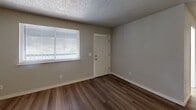 Located at 5429 Chicago Ave SW in Lakewood, WA, this single-floor unit offers three bedrooms, one bathroom, and a combined kitchen and living area. The open living space features wood-look laminate flooring and neutral-toned walls beneath a textured ceiling, with a window allowing natural light to fill the room. The galley-style kitchen is efficiently laid out with white cabinetry, dark granite-style countertops, a double-basin sink, and white appliances including a coil-top range, providing ample storage and counter space. The primary bedroom is a comfortable size and includes wood-look flooring, a large window with blinds, and direct access via a paneled door. The two additional bedrooms are carpeted and feature textured ceilings, neutral walls, and windows that bring in natural light. One bedroom includes a built-in closet with a double sliding door and shelving rod. The full bathroom is fitted with a combined tub and shower unit with chrome fixtures and wood-look flooring. Throughout the unit, six-panel doors, white trim, and a consistent neutral color palette contribute to a clean, functional aesthetic.