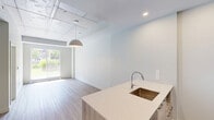 Located at 308 Rue Crevier in Saint-Laurent, Québec, this well-appointed one-bedroom, one-bathroom unit offers a thoughtfully designed layout with modern finishes throughout. Light wood-tone flooring flows seamlessly across the open living areas, complemented by crisp white walls that create a clean, contemporary aesthetic.

The kitchen serves as a functional centerpiece, featuring a large island with an integrated sink and quartz-style countertop, flat-front white upper cabinetry, wood-accented lower cabinets, a stainless steel refrigerator, and a built-in oven with an overhead range. Recessed lighting adds a polished finish overhead.

The open living area benefits from an exposed concrete ceiling and a large sliding glass door that draws in natural light and provides direct access to a private outdoor patio, offering views of surrounding greenery. A pendant light fixture anchors the space.

The bedroom is a bright, quiet retreat with a window overlooking lush outdoor foliage, a baseboard heater, and light-filled interiors. Exposed concrete ceiling details carry through from the main living area, adding an industrial touch.

The bathroom is finished to a high standard, with large-format grey floor tiles, a wall-mounted white vanity with an undermount sink, a wide mirror, and a frameless sliding glass shower enclosure. A dedicated closet provides additional storage just off the bathroom.