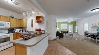Located at 1015 NW 21st Ave in Gainesville, Florida, this single-floor residence offers a well-organized and functional layout designed for comfortable everyday living. The open-concept common area seamlessly connects the kitchen, dining, and living spaces, creating a cohesive and sociable environment. The living room features carpet flooring, a ceiling fan, and a bold green accent wall that adds a lively pop of color, with a glass-top coffee table and ample natural light flowing in through large windows and a glass door leading outside. The kitchen is designed with a wraparound peninsula counter offering a granite-style surface, warm wood cabinetry, track lighting, and full-size appliances including a refrigerator and microwave. Tile flooring in the kitchen transitions smoothly into the carpeted living and dining areas. The residence includes multiple bedrooms, each with carpet flooring, ceiling fans, large windows with vertical blinds, and individual accent wall colors — including a soft blue and a muted mauve — giving each room a distinct character. The bathrooms are finished with tile flooring, granite-style vanity counters, and tub-shower combinations. A dedicated in-unit laundry room with side-by-side washer and dryer provides added convenience. Overall, the space presents a bright, practical, and inviting atmosphere throughout.