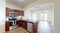 This single-story residence offers a well-designed, open-concept floor plan that seamlessly connects the kitchen and living areas. The kitchen is a standout feature, outfitted with rich mahogany-toned cabinetry, granite countertops, a stainless steel appliance suite including a refrigerator, range, microwave, and dishwasher, and a peninsula with a built-in sink. A dramatic arched passageway with track lighting defines the transition into the spacious living area, which features warm hardwood-style flooring, crown molding, and a ceiling fan with light fixture. French doors open to an outdoor area, allowing natural light to flow in and providing views of greenery beyond.

The bedroom is generously proportioned, featuring soft carpet, multiple windows, and a ceiling fan. It connects to a walk-in closet with multi-level wire shelving and carpeted flooring, offering ample storage. The bathroom is appointed with a granite-topped vanity, rich cabinetry matching the kitchen, a large mirror with modern lighting, and a full soaking tub with tiled surround. Hardwood-style flooring completes the bathroom. Throughout the space, neutral tones and consistent finishes create a cohesive and inviting atmosphere.