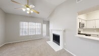 This single-story home offers a thoughtfully designed open layout with a cohesive neutral palette of soft grays and whites throughout. The living room serves as the heart of the home, distinguished by soaring vaulted ceilings that amplify the sense of space and a ceiling fan that adds both function and visual interest. A white-mantled fireplace with tile surround anchors the room, while large windows fitted with horizontal blinds allow natural light to fill the space. Plush wall-to-wall carpeting contributes to a warm, comfortable atmosphere.

The kitchen is open to the living area via a peninsula with white countertops, making it ideal for casual dining or entertaining. White shaker-style cabinetry, a classic subway tile backsplash, and stainless steel appliances—including a range, microwave, and refrigerator—combine practicality with a clean, modern aesthetic. Light wood-look flooring grounds the kitchen space.

The bedroom continues the vaulted ceiling design, complemented by a ceiling fan and a window that brings in natural light. The bathroom features a wide vanity with white cabinetry, a framed mirror, and light tile flooring, offering a functional and tidy finish.