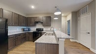 Located at 4950 Weaver Rd in Lake Charles, Louisiana, this single-story 2-bedroom, 1-bathroom home offers a thoughtfully designed layout with modern finishes throughout. The open-concept kitchen and living area serves as the heart of the home, featuring rich dark-stained cabinetry, granite-look countertops, black appliances, and a central island with a built-in sink and stylish pendant lighting — ideal for both cooking and entertaining. Wood-look plank flooring runs throughout the entire home, providing a warm, cohesive aesthetic. The living area is generously sized and filled with natural light from large windows. The primary bedroom offers a comfortable amount of space, a ceiling fan, and natural light from a window with outdoor views, along with two closets for ample storage. The second bedroom also features a ceiling fan and access to natural light. The shared bathroom is well-finished with dark cabinetry, granite countertops, and a large mirror. A hallway connects the living spaces to the bedrooms and bathroom, providing a practical and efficient flow. Neutral gray-toned walls throughout complement the warm flooring, creating a clean and inviting ambiance well-suited to a variety of interior styles.