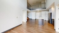 Located at 120 Border St in Boston's East Boston neighborhood, this two-story residence offers five bedrooms, two bathrooms, and generous living space spread across two well-proportioned floors. The main level immediately impresses with soaring double-height ceilings that flood the open-concept living and kitchen area with natural light. The modern kitchen features sleek white cabinetry, stainless steel appliances, and a central island with an integrated sink, complemented by large sliding glass doors that open to views of the surrounding community courtyard. Warm hardwood-style flooring runs throughout both levels, adding continuity and character. A striking staircase with wood handrails and contemporary metal mesh railings connects the floors, leading to an upper-level hallway that overlooks the main living area below. The five bedrooms are well-sized, including a primary bedroom with its own closet, while three dedicated closets throughout provide ample storage. The two bathrooms are finished with neutral tilework — one featuring a glass-enclosed walk-in shower and modern floating vanity, the other a full soaking tub and subway tile surround. Bedrooms on the upper floor enjoy urban views of the Boston skyline and neighboring architecture through large, bright windows.