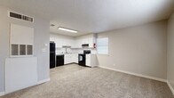 This efficient single-floor unit offers a thoughtfully arranged layout encompassing a kitchen, living area, bedroom, bathroom, and closet. The open kitchen is a standout feature, outfitted with crisp white shaker-style cabinetry, light stone countertops, a white subway tile backsplash, and a full suite of black appliances including a refrigerator, electric range with overhead ventilation, and dishwasher. Light wood-look flooring runs throughout the kitchen, transitioning to neutral-toned carpet in the living and bedroom areas, creating a warm and cohesive feel. The living space is open to the kitchen, offering a functional and connected layout. The bedroom provides a comfortable retreat with a ceiling fan with light fixture, a window allowing natural light, and carpeted flooring. A dedicated closet offers practical storage. The bathroom is clean and functional, featuring a white vanity with a speckled countertop, a full tub-shower combination with white tile surround, and wood-look flooring. Neutral gray walls, textured ceilings, and white trim are consistent throughout, giving the unit a clean, uniform aesthetic suited for everyday living.