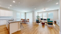 This single-floor home offers a thoughtfully designed open-concept layout that seamlessly connects the kitchen, dining, and living areas. The kitchen is appointed with crisp white cabinetry, granite countertops, stainless steel appliances, and a central island with bar seating — ideal for both everyday cooking and entertaining. Adjacent to the kitchen, the dining area accommodates a full-sized table and benefits from natural light streaming through multiple windows and a sliding glass door. The living room is a comfortable, airy space featuring a ceiling fan, large windows with blinds, and warm light wood flooring that runs consistently throughout the home. A dedicated home office provides a bright, functional workspace with natural light from a window. The master bedroom is generously proportioned with tray ceilings, crown molding, and direct access to a private en-suite bathroom featuring a dual-sink granite vanity, white cabinetry, and a walk-in shower. The entryway offers a welcoming introduction to the home with recessed lighting and a clean, neutral palette. Throughout, light-toned walls, wood-look flooring, and recessed lighting create a cohesive, modern aesthetic that is both practical and inviting.
