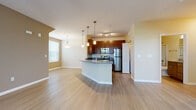 This single-story residence in North Port, Florida, presents a well-designed open-concept layout that seamlessly connects the living, dining, and kitchen areas. Light-toned wood-style flooring flows throughout the main living spaces, creating a cohesive and airy feel, while neutral warm-beige walls complement the overall design.

The kitchen serves as a central focal point, anchored by a curved peninsula with granite countertops that provides both workspace and a casual dining option. Rich dark-wood cabinetry offers generous storage, while a full suite of stainless steel appliances—including a refrigerator, range, microwave, and dishwasher—adds a modern, polished touch. Pendant lighting hangs above the peninsula, adding functional style to the space.

The living area benefits from natural light through a large sliding glass door that opens to an outdoor area, accompanied by a ceiling fan overhead. Bedrooms feature plush carpeting and windows with blinds that allow controllable natural light. The bathrooms are finished with matching granite-topped dark-wood vanities and light wood-style flooring, with one bathroom offering a tub-shower combination enclosed by sliding glass doors.