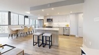Located at 8 Silver Maple Crt in Brampton, Ontario, this well-appointed one-bedroom, one-bathroom unit offers a thoughtfully designed open-concept layout bathed in natural light. Light-toned hardwood flooring flows seamlessly throughout, complementing the unit's clean, contemporary aesthetic.

The open-concept living, dining, and kitchen area forms the heart of the space. The modern kitchen is outfitted with two-tone cabinetry — white upper cabinets paired with warm wood lower cabinets — along with stainless steel appliances, a white quartz countertop, subway tile backsplash, and a central island with bar seating. The dining area benefits from floor-to-ceiling windows that frame expansive outdoor views of the Brampton skyline, flooding the space with natural light. The living room continues this bright, airy character with large windows and a neutral palette.

The generously sized primary bedroom features a large window with sweeping city views, light hardwood flooring, and a calm, restful atmosphere. The bathroom is finished with clean white tile and a full soaker tub. A welcoming hallway connects all areas of the unit with ease. Recessed lighting and soft grey walls throughout lend the space a polished, modern character.