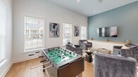 Located at 157 Hathaway Ln in Mooresville, NC, this single-story amenity space offers a generously sized, open-concept layout designed for gathering, relaxation, and recreation. The interior is finished with warm-toned hardwood flooring throughout, crisp white walls, and elevated ceilings that contribute to an airy, welcoming atmosphere.

The space is organized into distinct functional areas that flow seamlessly into one another. A stylish lounge area features plush seating arrangements set atop vibrant geometric area rugs, anchored by a bold teal accent wall with a wall-mounted flat-screen TV and a built-in wood ledge shelf. Recessed lighting and large windows with white blinds allow abundant natural light to fill the room, offering views of the surrounding community.

A dedicated game room area accommodates a full-size pool table and a foosball table, providing ample entertainment options. This section benefits from multiple windows that brighten the space and create an inviting environment for play.

A separate sitting area with additional lounge seating and colorful area rugs offers a quieter retreat within the space. The overall design blends modern furnishings with clean architectural lines, creating a cohesive, contemporary aesthetic throughout. The space is well-suited for community socializing and recreational activities.