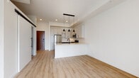 This single-floor unit showcases a thoughtfully designed open-concept layout, where the kitchen and living area flow seamlessly together. Light wood-tone flooring runs throughout, creating a warm, cohesive aesthetic against crisp white walls and ceilings fitted with recessed lighting.

The kitchen is a standout feature, combining two-tone cabinetry—dark lower cabinets paired with light upper cabinets accented by matte black hardware—alongside a herringbone tile backsplash. A full suite of stainless steel appliances includes a gas range, over-range microwave, and a full-size refrigerator. A peninsula with a light countertop and an undermount sink with a matte black faucet provides additional prep space and seating potential. Three pendant lights hang above, adding a stylish focal point.

The living area is bright and airy, benefiting from a large window that frames striking urban skyline views. A barn-style sliding door adds a modern architectural touch near the entryway.

The bathroom features a clean, minimalist design with white subway tile surrounding the tub-shower combination, light wood flooring, a white vanity with ample storage, and coordinating matte black fixtures throughout.

A dedicated laundry closet houses a stacked washer and dryer, adding practical convenience to the unit's overall functional design.