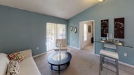 This single-story unit at 9300 SW 137 Avenue offers a functional and well-organized layout. The living room is a standout space, featuring vaulted ceilings, a teal accent wall, and sliding glass doors that allow natural light to pour in while providing views of the outdoors. Carpet flooring runs throughout the living and sleeping areas, adding warmth underfoot.

The kitchen is positioned adjacent to the living area and features a pass-through counter that opens to the main living space. White cabinetry, a built-in microwave, and a range are housed beneath a distinctive wood-toned overhead cabinet, while light tile flooring carries through the kitchen and entry areas.

The bedroom is a comfortable retreat with a ceiling fan, carpeted floors, and a dedicated closet. Windows dressed with vertical blinds allow natural light while maintaining privacy. The room connects directly to the bathroom, which includes a wide vanity with ample counter space, wood-trimmed cabinetry, a large framed mirror, and a Hollywood-style light bar above the sink. A separate toilet and shower area complete the bathroom.

Overall, the unit presents a clean, neutral palette with teal accent walls providing a cohesive design element throughout the space.