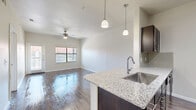 Located at 7035 Pickwell Dr in San Antonio, TX, this one-bedroom, one-bathroom residence offers a thoughtfully designed layout with modern finishes throughout. The open-concept living and kitchen area serves as the heart of the home, featuring rich wood-style flooring that extends across the main living spaces. A ceiling fan with integrated lighting adds comfort and functionality to the living room, which also benefits from natural light streaming through large windows and access to an outdoor area.

The kitchen is a standout feature, showcasing granite countertops, dark espresso cabinetry, a tile backsplash, and a full suite of stainless steel appliances including a refrigerator, electric range, and built-in microwave. A peninsula with an undermount sink and pendant lighting above adds both prep space and a casual dining option.

The bedroom offers a comfortable, carpeted retreat with a ceiling fan, a well-sized window with exterior views, and direct access to both a closet and the bathroom. The bathroom continues the home's cohesive design with granite countertops, dark cabinetry, an undermount sink, and wood-style tile flooring. A hallway connects the bedroom and bathroom, completing the efficient and functional floor plan of this San Antonio residence.