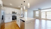 This single-floor residence offers a thoughtfully designed layout encompassing three bedrooms, two bathrooms, and three closets. The open-concept kitchen and living area serves as the heart of the home, finished with warm hardwood-style flooring that carries throughout the main living spaces. The kitchen is outfitted with white shaker cabinetry, stone-topped counters, a central island with an undermount sink and matte black faucet, and a full suite of stainless steel appliances. Pendant lighting above the island and recessed ceiling lights add layered illumination. The adjacent living area features a ceiling fan and natural light from multiple windows.

The bedrooms are carpeted and neutral in tone, with the primary bedroom benefiting from multiple windows and a ceiling fan. A walk-in closet with built-in shelving and hanging rods provides organized storage. Both bathrooms echo the kitchen's design language, featuring white cabinetry, stone-topped vanities, matte black hardware, large mirrors, and tub-shower combinations with tile surrounds and hardwood-style flooring, creating a cohesive, modern aesthetic throughout.